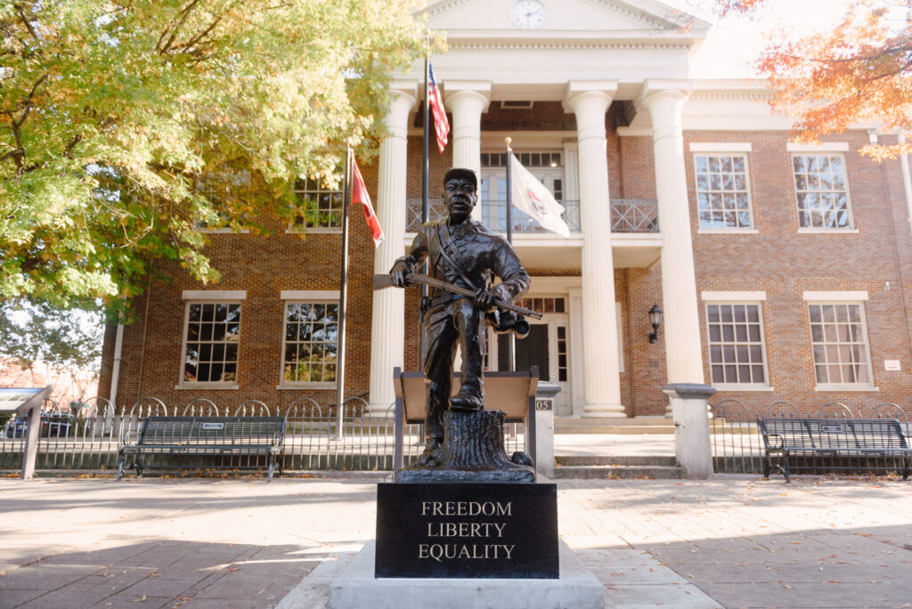 A bronze statue of a soldier stands in front of a historic brick building with columns in Williamson County, Tennessee.
