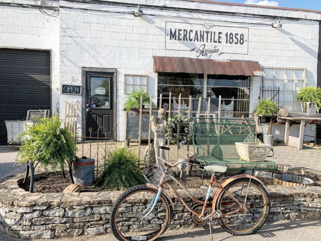 A vintage bicycle leans against a stone wall outside an antique shop with a rustic, shabby chic aesthetic in Williamson County, Tennessee.