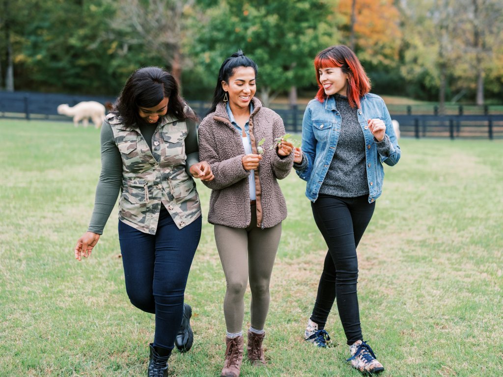 Three women walk together in a grassy field, smiling and holding hands in Williamson County, Tennessee.