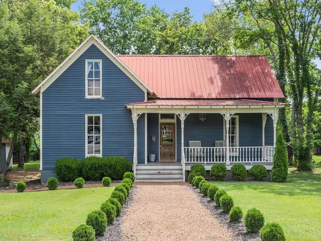 A charming blue farmhouse with white trim and a red roof sits on a well-manicured lawn in Williamson County, Tennessee.