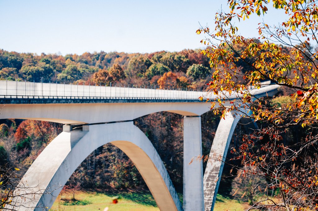 A white concrete bridge with three large arches spans a valley, surrounded by colorful autumn trees in Williamson County, Tennessee.