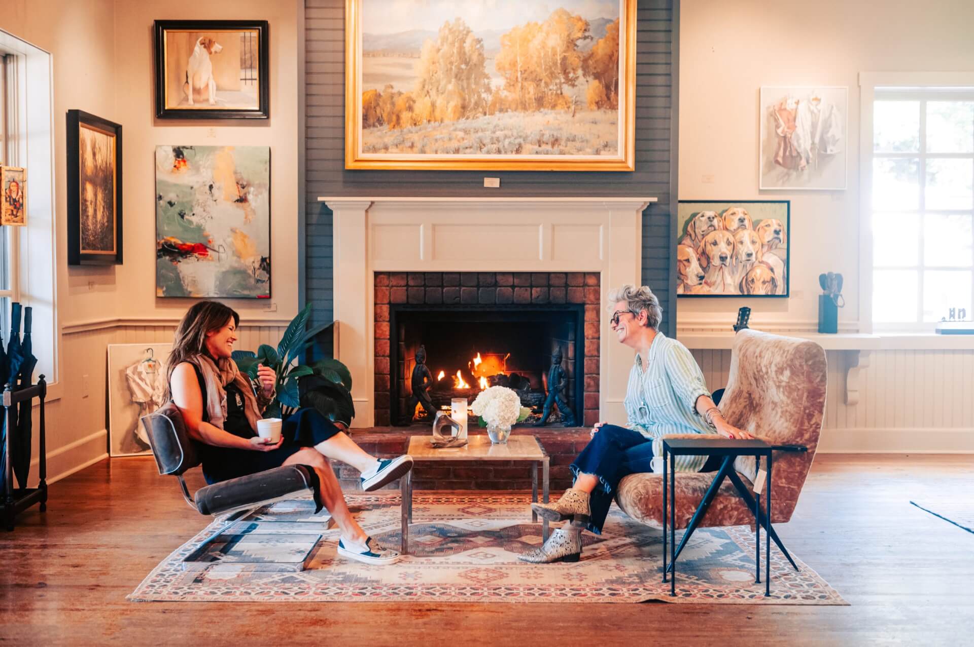 Two women in stylish chairs chat by a cozy fireplace in an art-filled room in Williamson County, Tennessee.