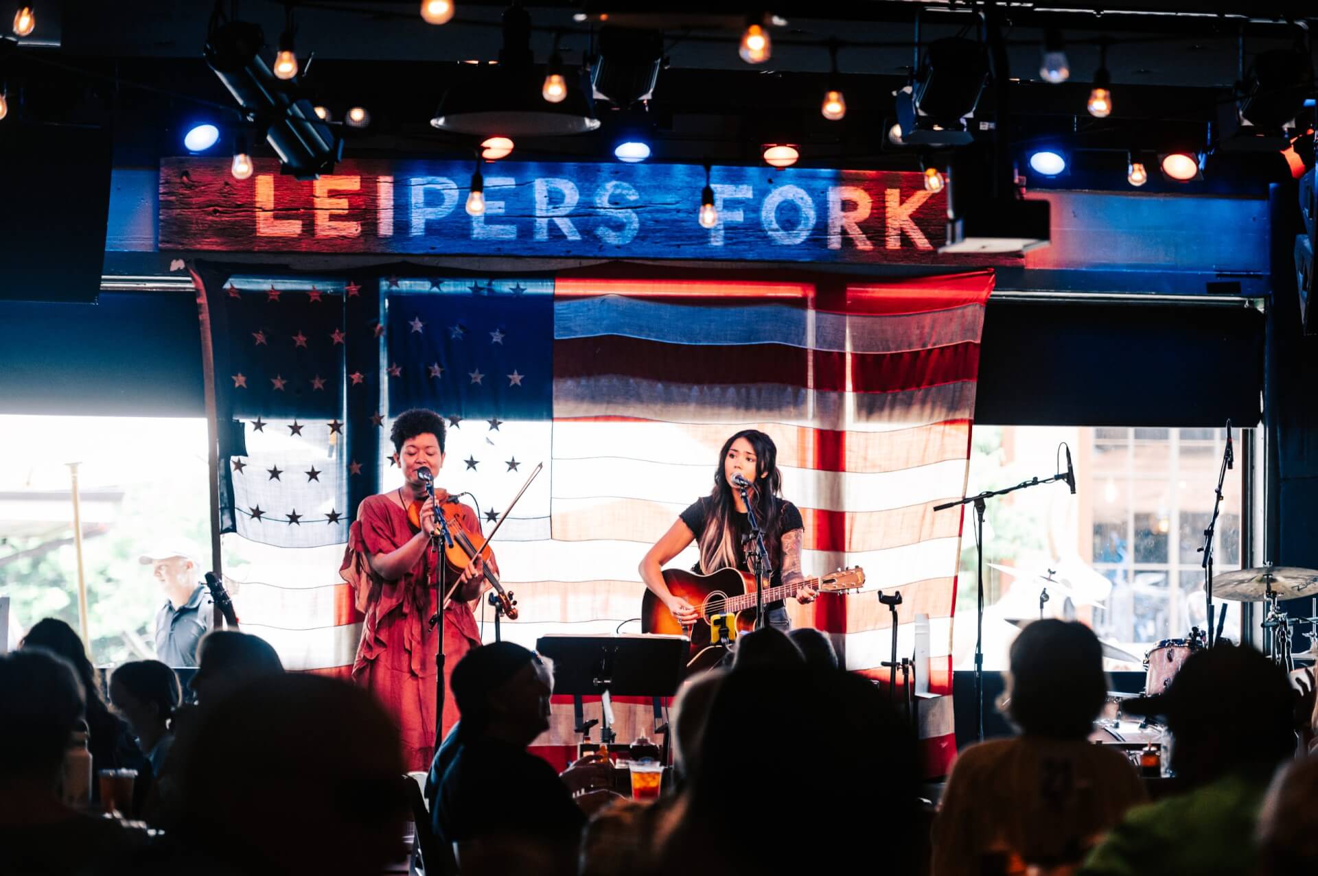 Two musicians perform on stage with an American flag backdrop at a lively music venue in Williamson County, Tennessee.