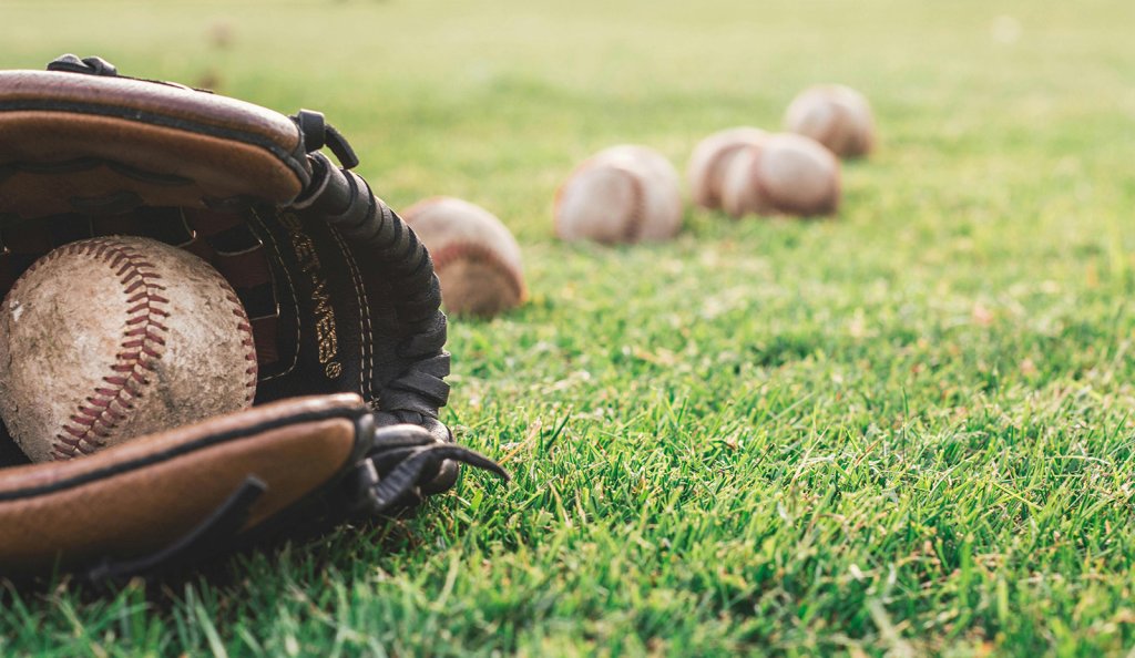Closeup of baseball mitt and baseballs laying in grass