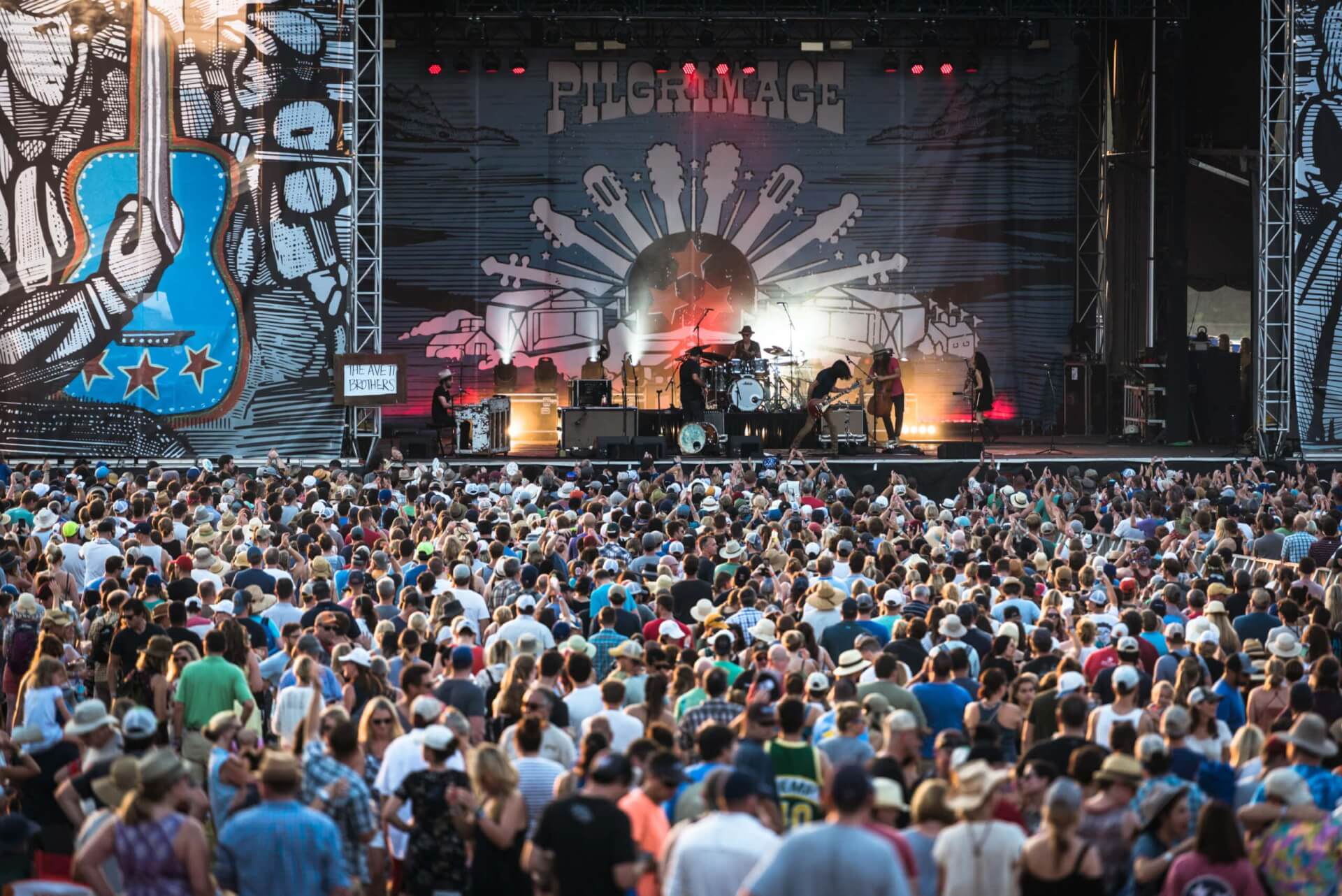 A massive crowd at an outdoor music festival watches a band perform on a large stage with colorful lighting in Williamson County, Tennessee.