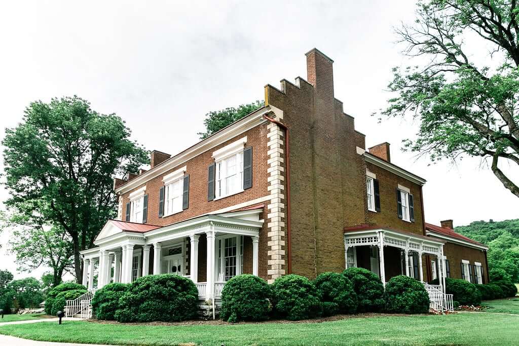 A stately red brick mansion with white columns and a wrap-around porch stands amidst lush greenery in Williamson County, Tennessee.