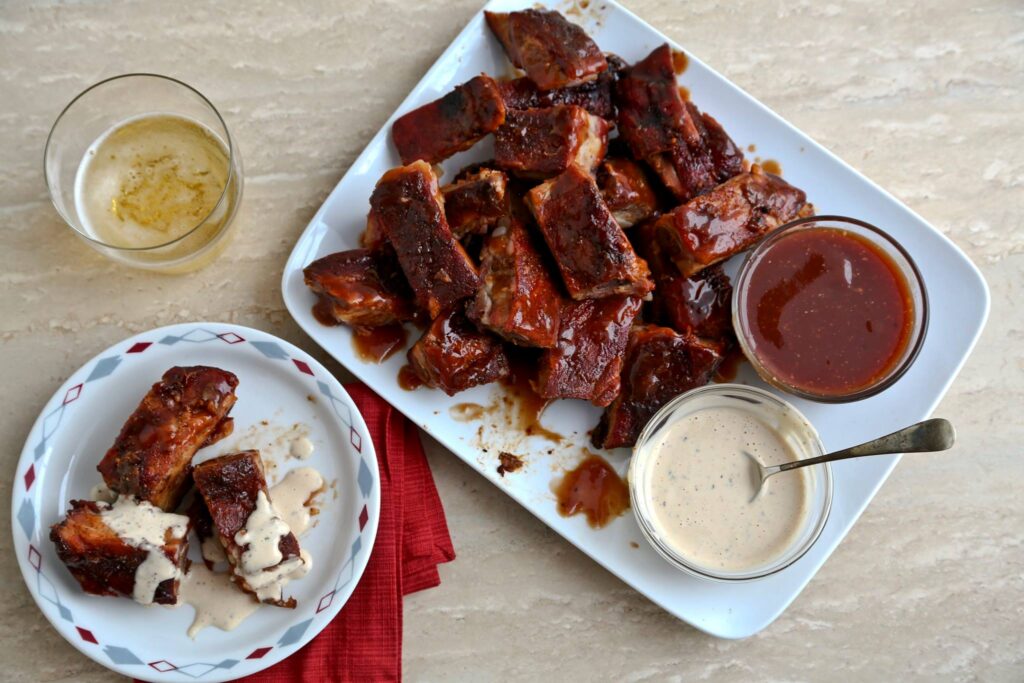 A plate of barbecue ribs with dipping sauces and a glass of beer on a wooden table in Williamson County, Tennessee.