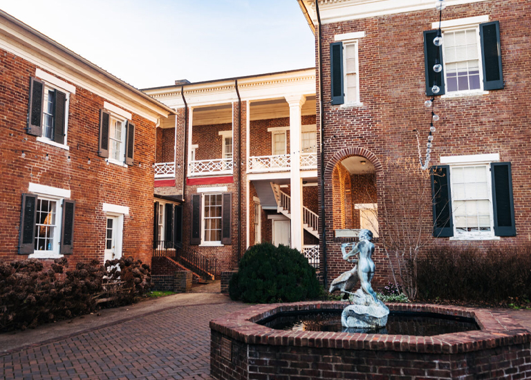 A courtyard with a brick fountain featuring a statue of a woman, surrounded by red brick buildings with white columns and shutters in Williamson County, Tennessee.