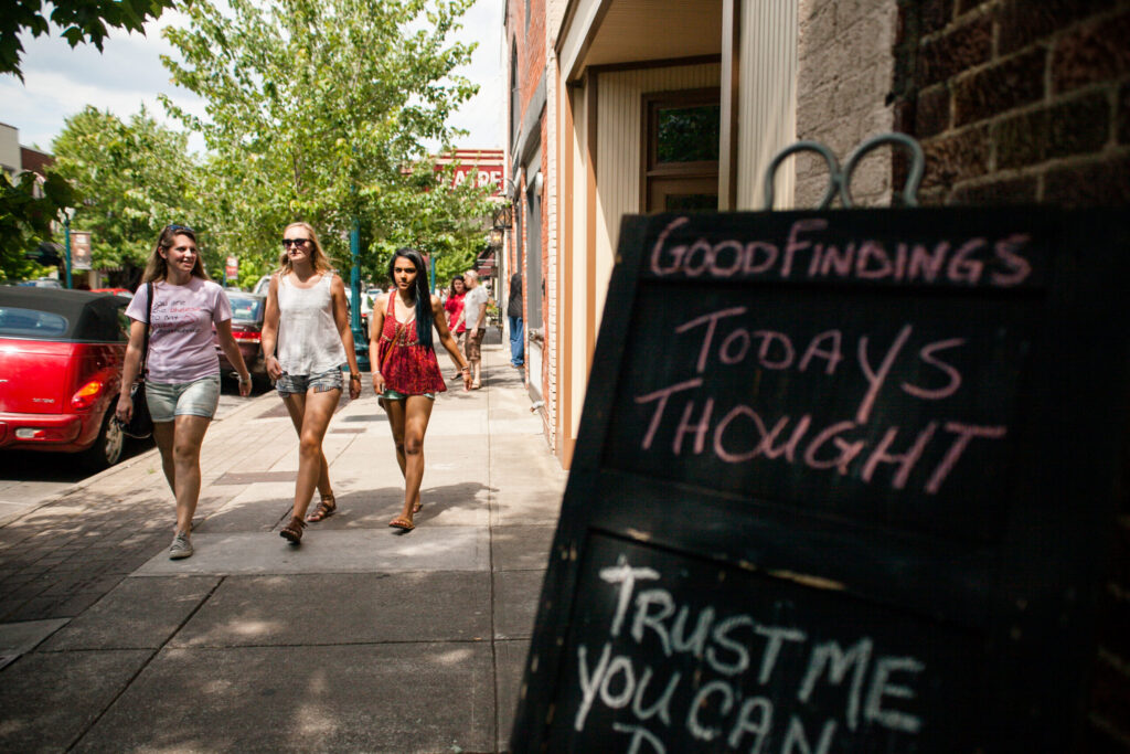 Three women walk down a sunny sidewalk past a chalkboard sign with inspirational quotes in Williamson County, Tennessee.