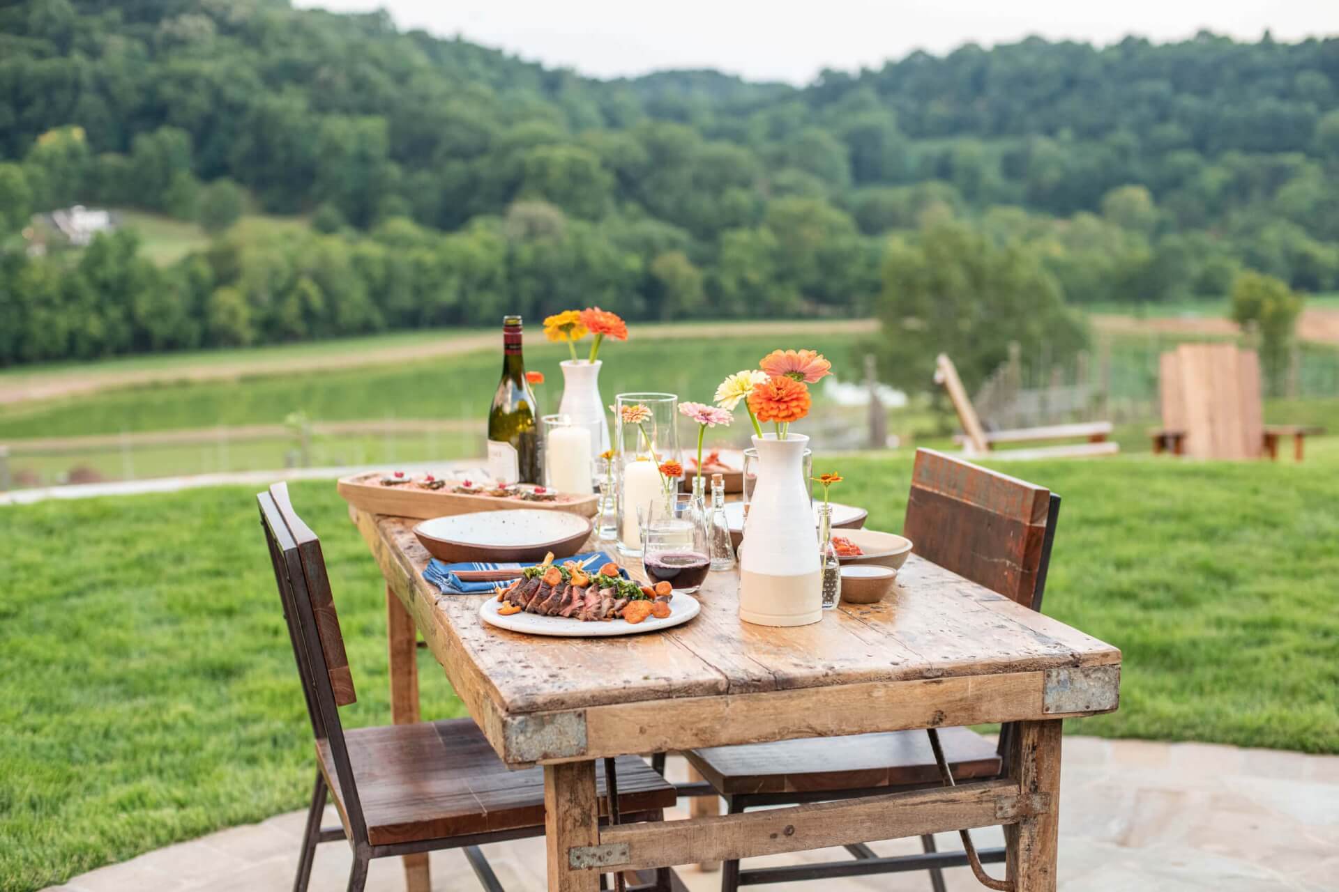 Rustic wooden table set for outdoor meal with food, wine, and flowers in Williamson County, Tennessee.
