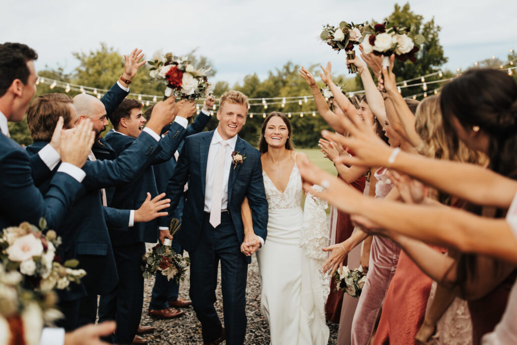 A joyful bride and groom walk down the aisle, surrounded by clapping guests holding flower bouquets in Williamson County, Tennessee.