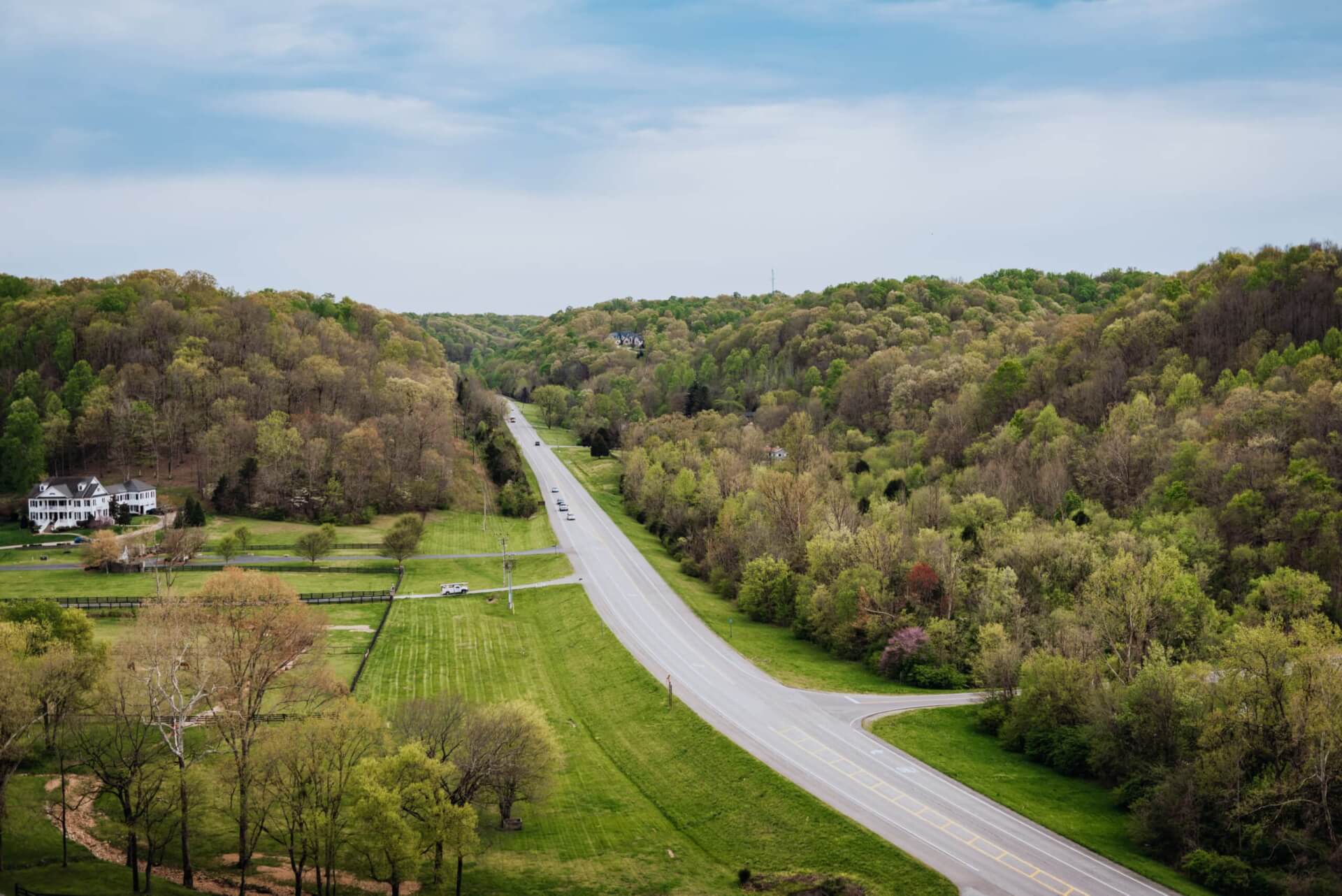 A winding road cuts through a lush, green forest with patches of farmland in Williamson County, Tennessee.