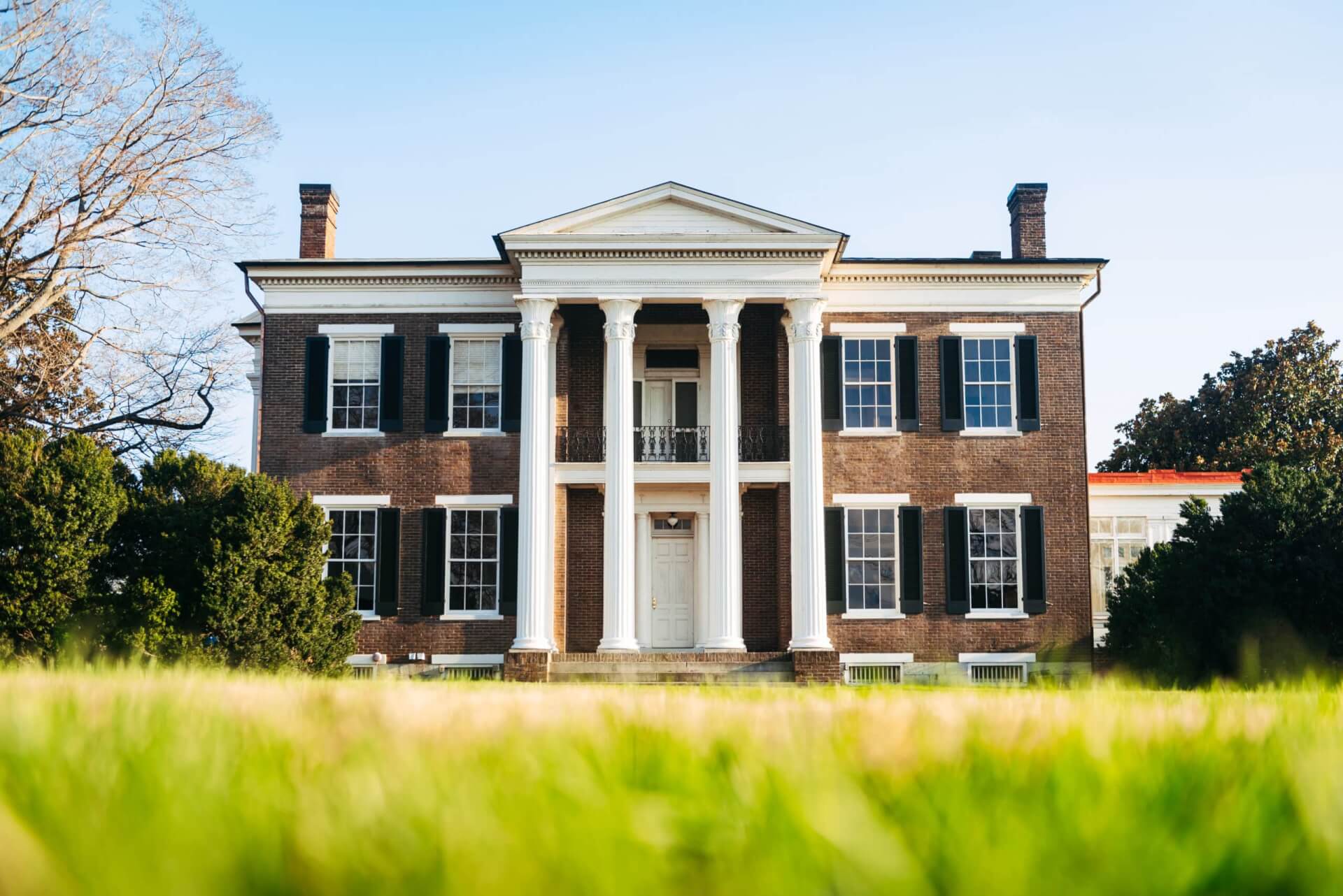 A stately brick mansion with white columns and a grand entrance stands amidst lush greenery in Williamson County, Tennessee.