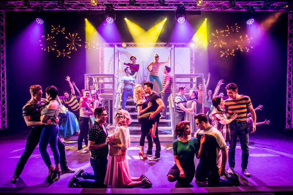 A vibrant stage performance featuring a large cast in colorful 1950s attire dancing and singing in Williamson County, Tennessee.