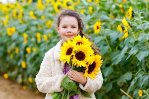 A young girl with a braid holds a bouquet of vibrant sunflowers in a field in Williamson County, Tennessee.