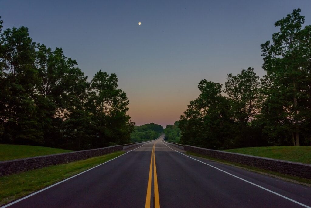 A winding two-lane road stretches into the distance, flanked by lush green trees and a stone wall in Williamson County, Tennessee.