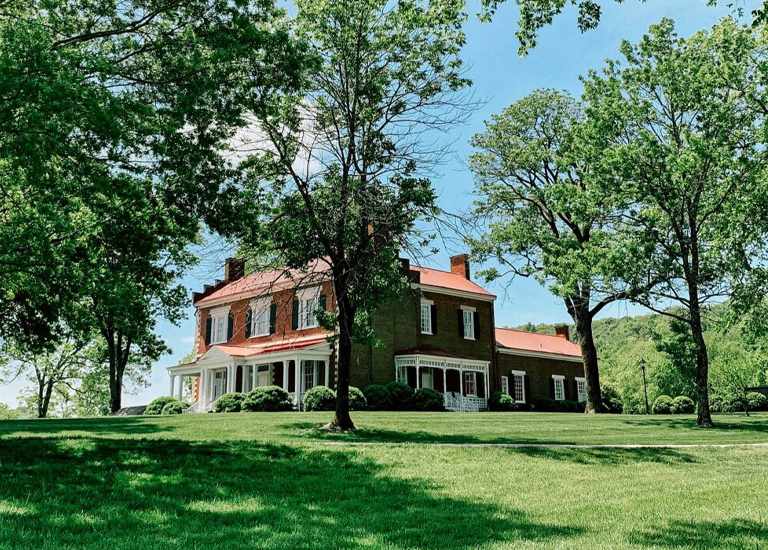 A large red-roofed house with white columns and shutters is nestled among lush green trees in Williamson County, Tennessee.