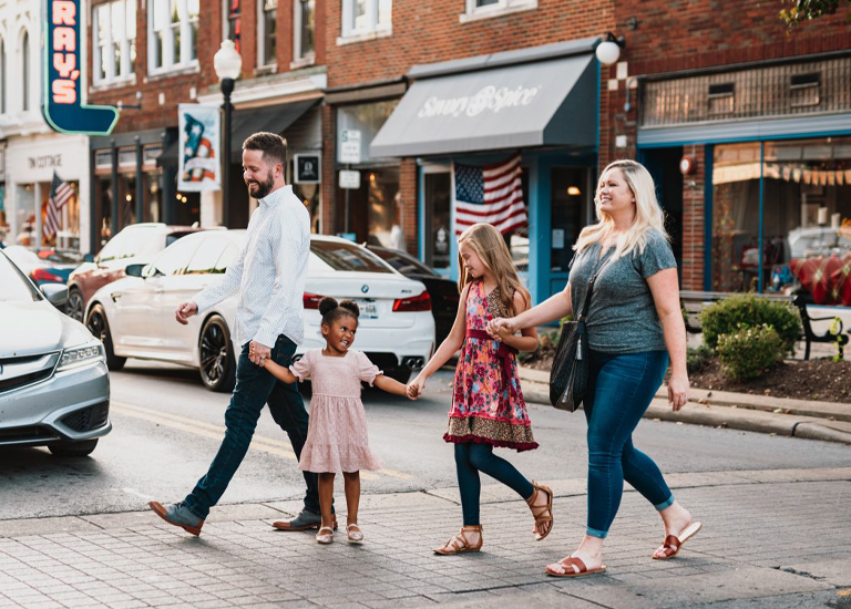 A family of four, including two young girls, walks hand-in-hand across a street in a small town in Williamson County, Tennessee.