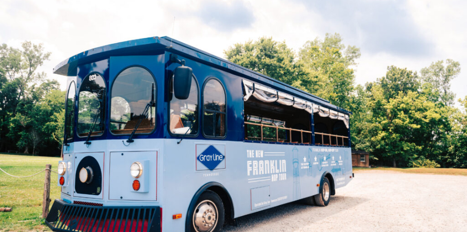 A blue trolley-style tour bus with open sides and a canopy is parked on a gravel path in Williamson County, Tennessee.