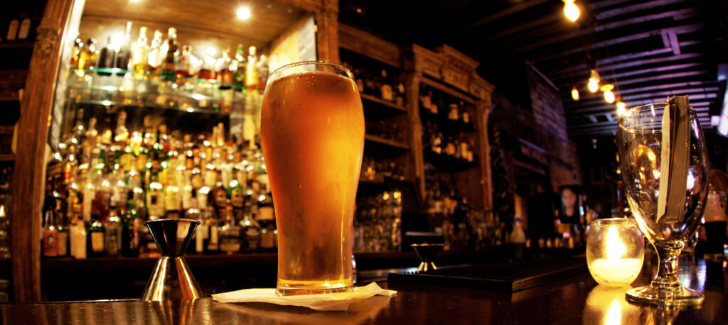 A tall glass of golden beer sits on a bar counter, illuminated by warm candlelight in Williamson County, Tennessee.