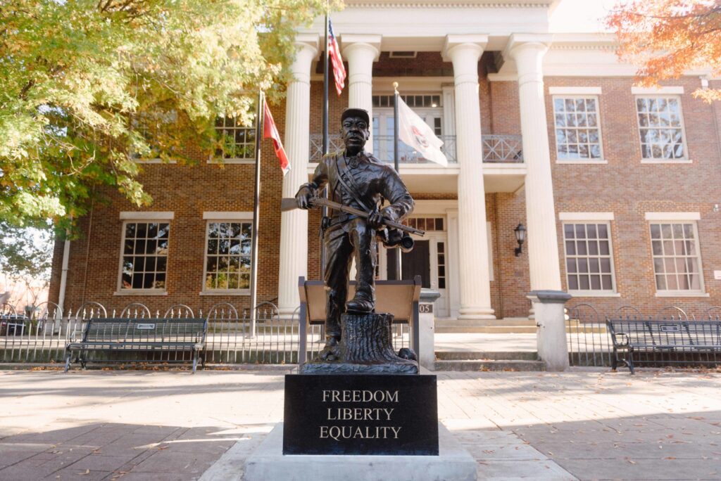 A statue of a soldier stands in front of a brick building with columns and flags in Williamson County, Tennessee.