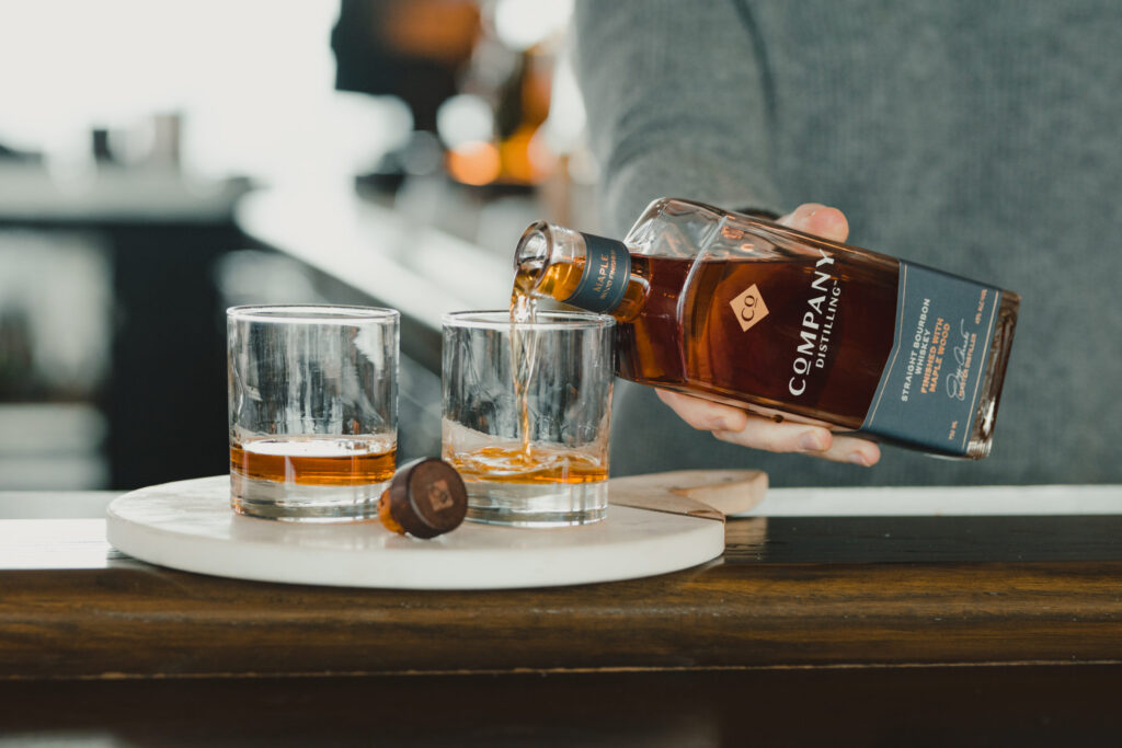 A person pours whiskey from a bottle into two glasses on a marble tray at a bar in Williamson County, Tennessee.
