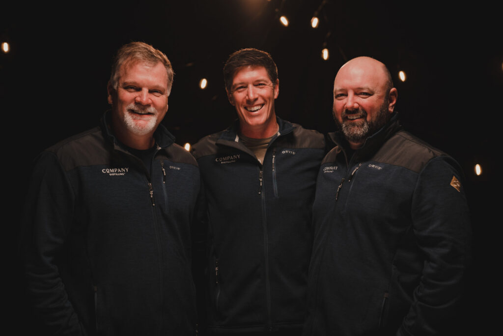 Three smiling men in matching jackets stand together against a dark background in Williamson County, Tennessee.