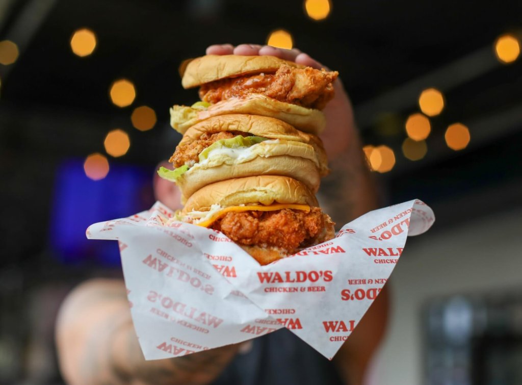 A person holds three stacked chicken sandwiches wrapped in branded paper in Williamson County, Tennessee.