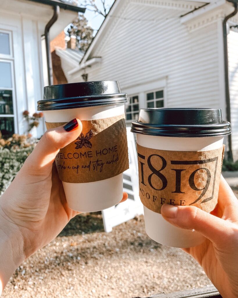 Two hands hold coffee cups with 'Welcome Home' and '1819 Coffee' branding in Williamson County, Tennessee.