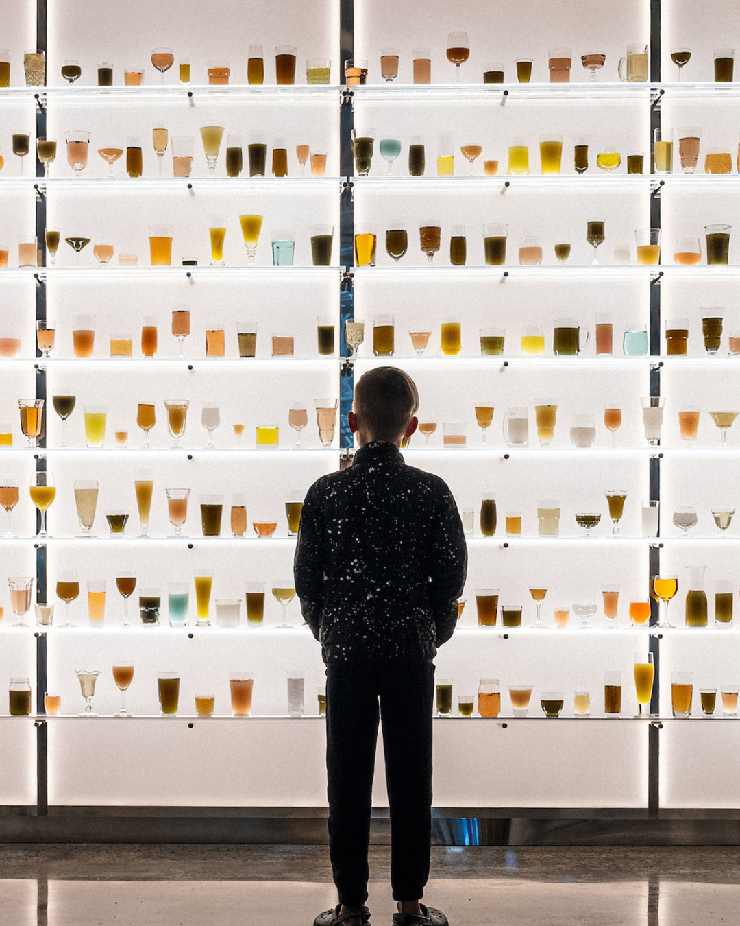 A child stands in front of a wall filled with colorful glasses of various liquids in Williamson County, Tennessee.