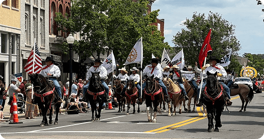 The Franklin Rodeo A parade featuring a group of riders on horseback, each carrying flags, marches down a town street lined with spectators in Williamson County, Tennessee.