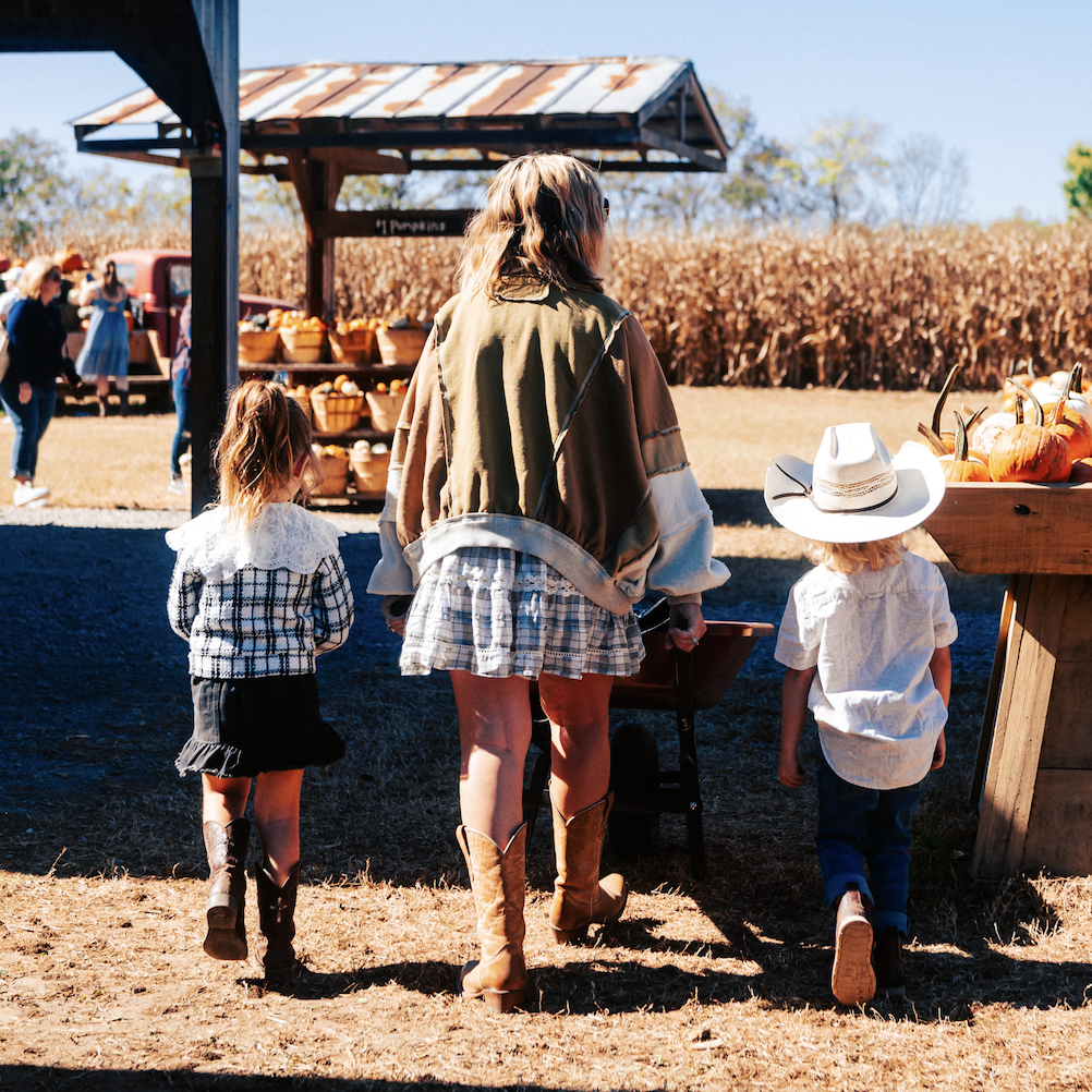 A family of three, dressed in cowboy attire, walks through a pumpkin patch on a sunny day in Williamson County, Tennessee.