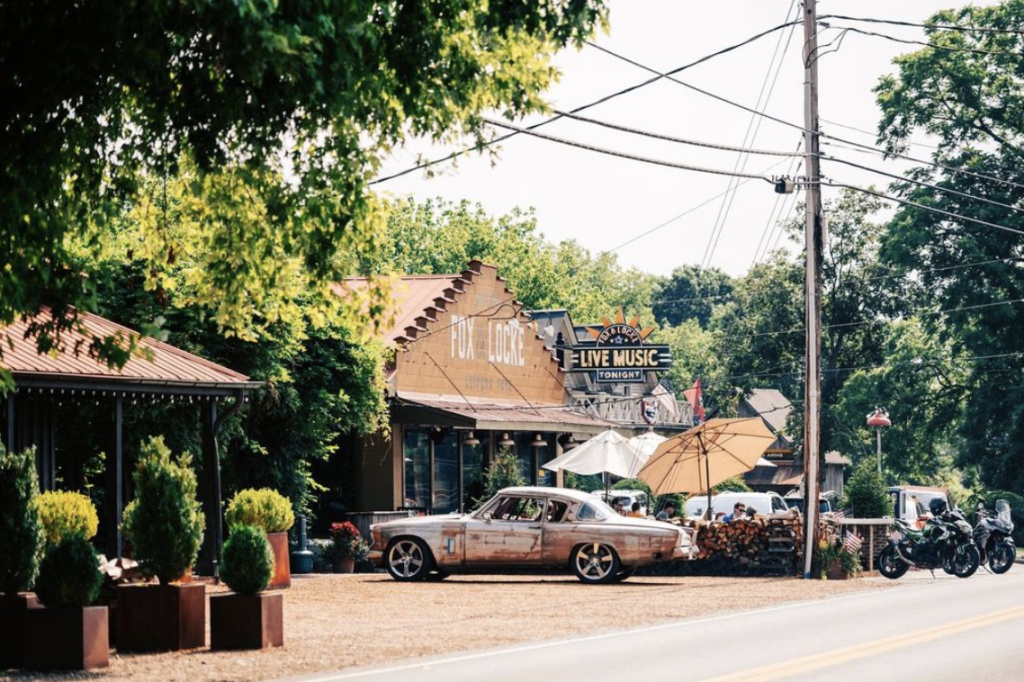 A vintage car sits outside a live music venue with outdoor seating and umbrellas in Williamson County, Tennessee.
