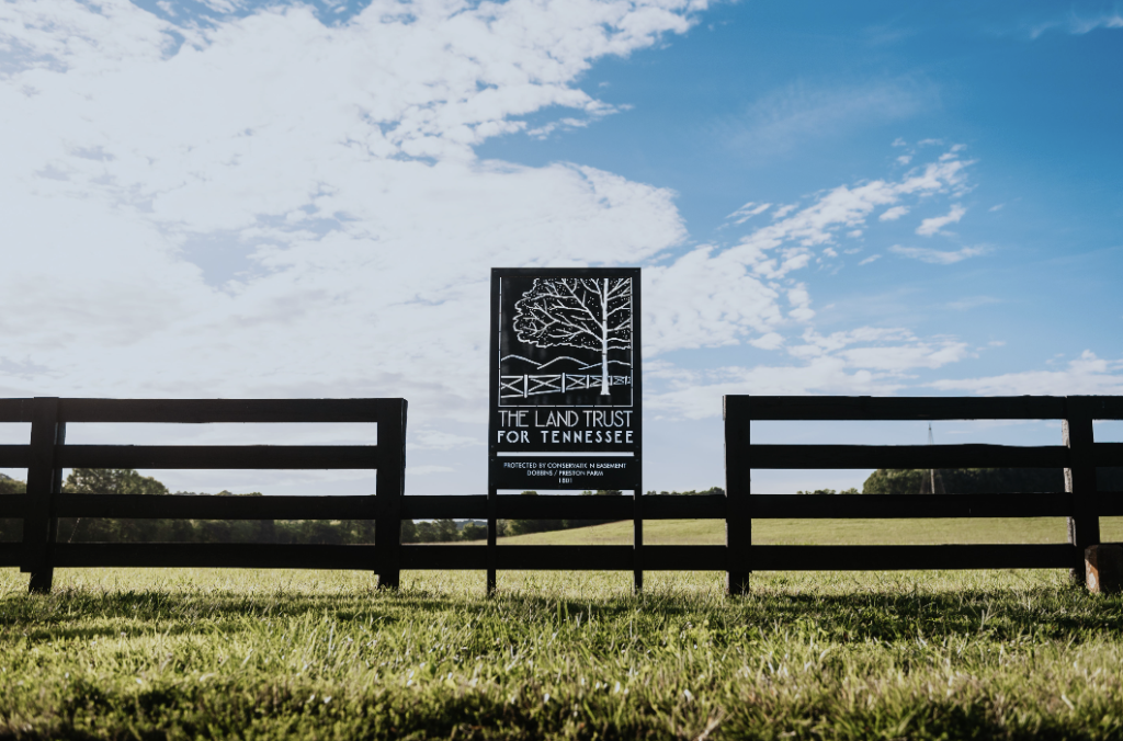 A black fence with a sign for The Land Trust for Tennessee in a grassy field in Williamson County, Tennessee.