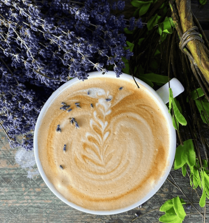 A steaming cup of lavender latte art sits on a wooden table with fresh lavender sprigs in Williamson County, Tennessee.