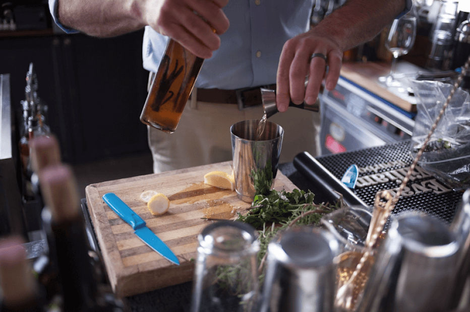 A bartender pours a liquid from a bottle into a cocktail shaker on a wooden cutting board in Williamson County, Tennessee.