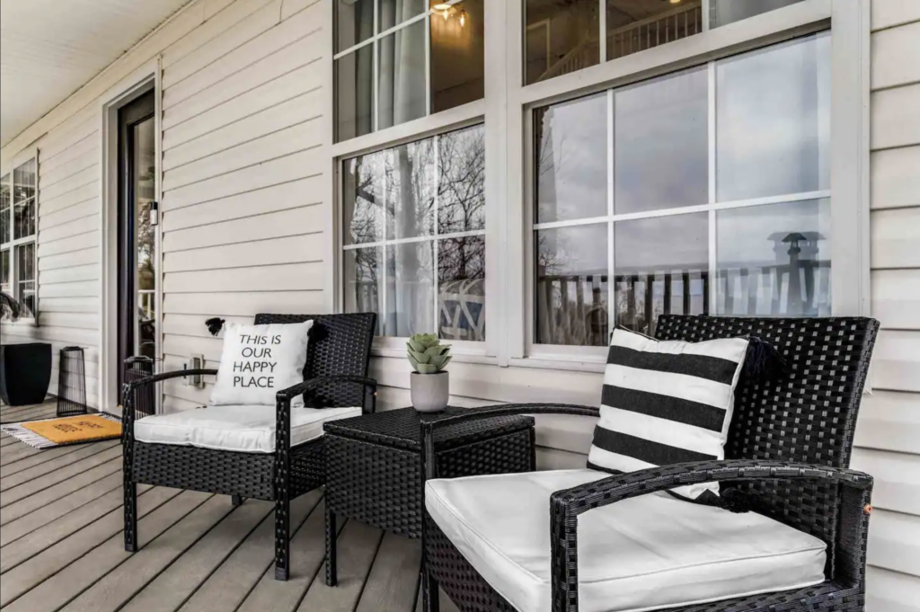 Black wicker patio furniture with white cushions on a wooden deck outside a white house in Williamson County, Tennessee.