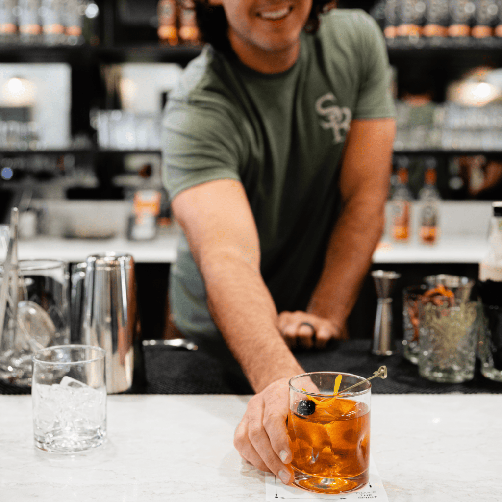 A bartender with long hair is preparing a cocktail in a dimly lit bar in Williamson County, Tennessee.