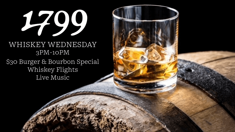 A glass of whiskey with ice cubes sits on a wooden barrel with metal hoops in Williamson County, Tennessee.